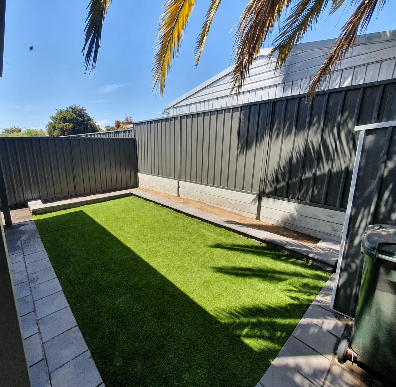 Backyard after landscaping with fresh artificial turf and paved borders
